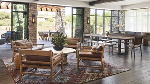 A spacious indoor area with a stone accent wall, wooden furniture, and large windows offering a view of the outdoors. - The Eddy Hotel Tucson, Tapestry Collection By Hilton (Tucson)