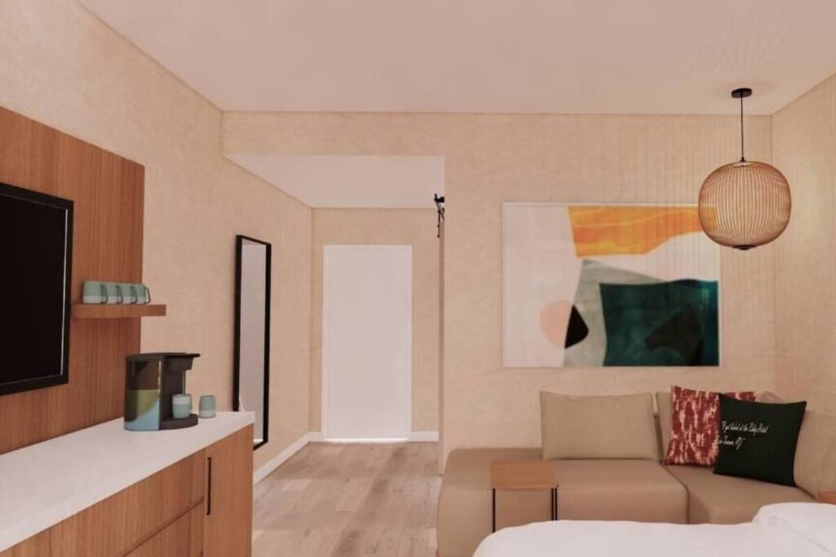 A modern hotel room with a bed, a sofa, a TV, a coffee machine, and a painting on the wall.