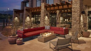 A modern outdoor living area with a stone facade, a red sofa, a fire pit, and outdoor furniture. - The Eddy Hotel Tucson, Tapestry Collection By Hilton (Tucson)