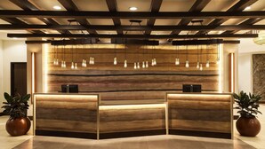 A reception desk with a wooden finish, multiple light fixtures, and two potted plants. - The Eddy Hotel Tucson, Tapestry Collection By Hilton (Tucson)