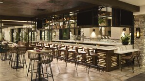 A bar area with high stools and a long counter, surrounded by stone walls and shelves with bottles. - The Eddy Hotel Tucson, Tapestry Collection By Hilton (Tucson)