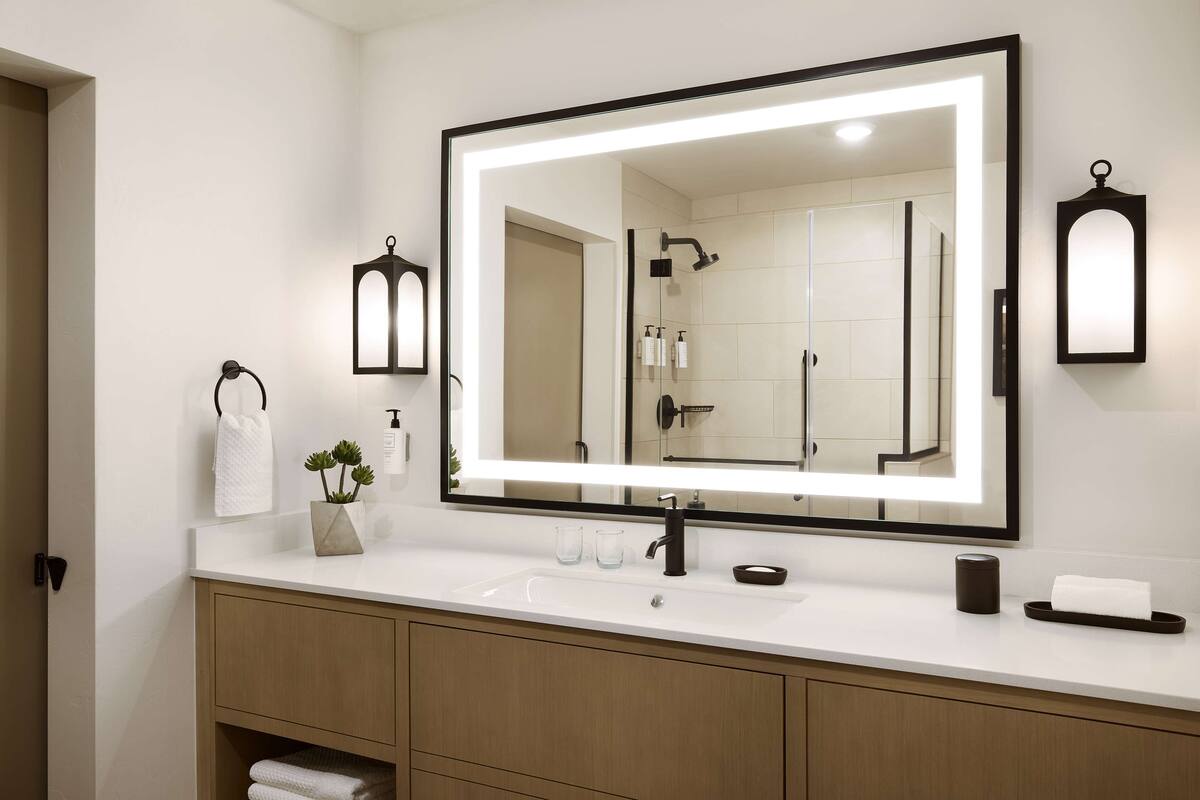 A modern bathroom with a large mirror, white sink, and wooden vanity.