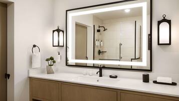A modern bathroom with a large mirror, white sink, and wooden vanity.