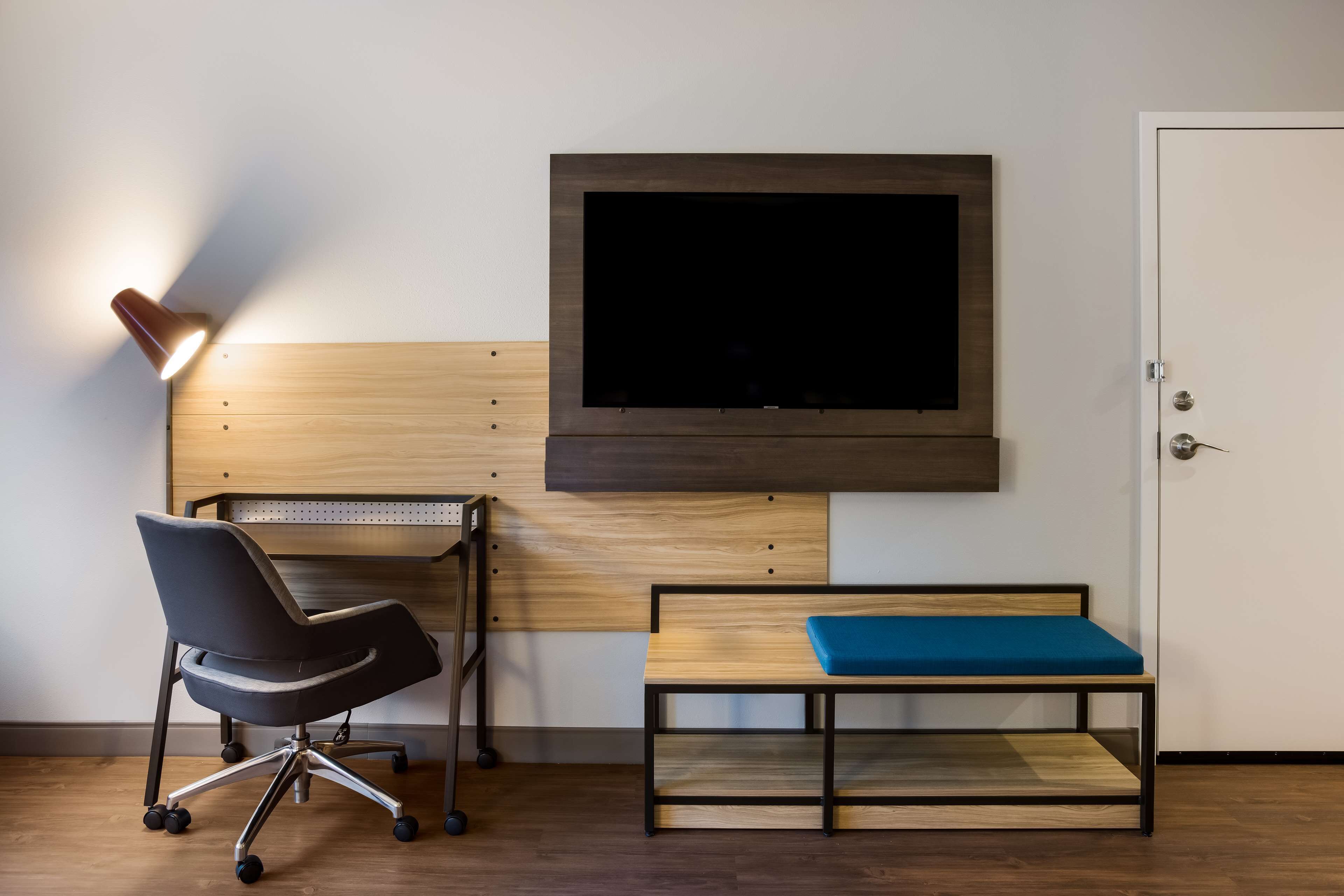 Una habitación moderna con escritorio, silla, banco y televisor montado.
