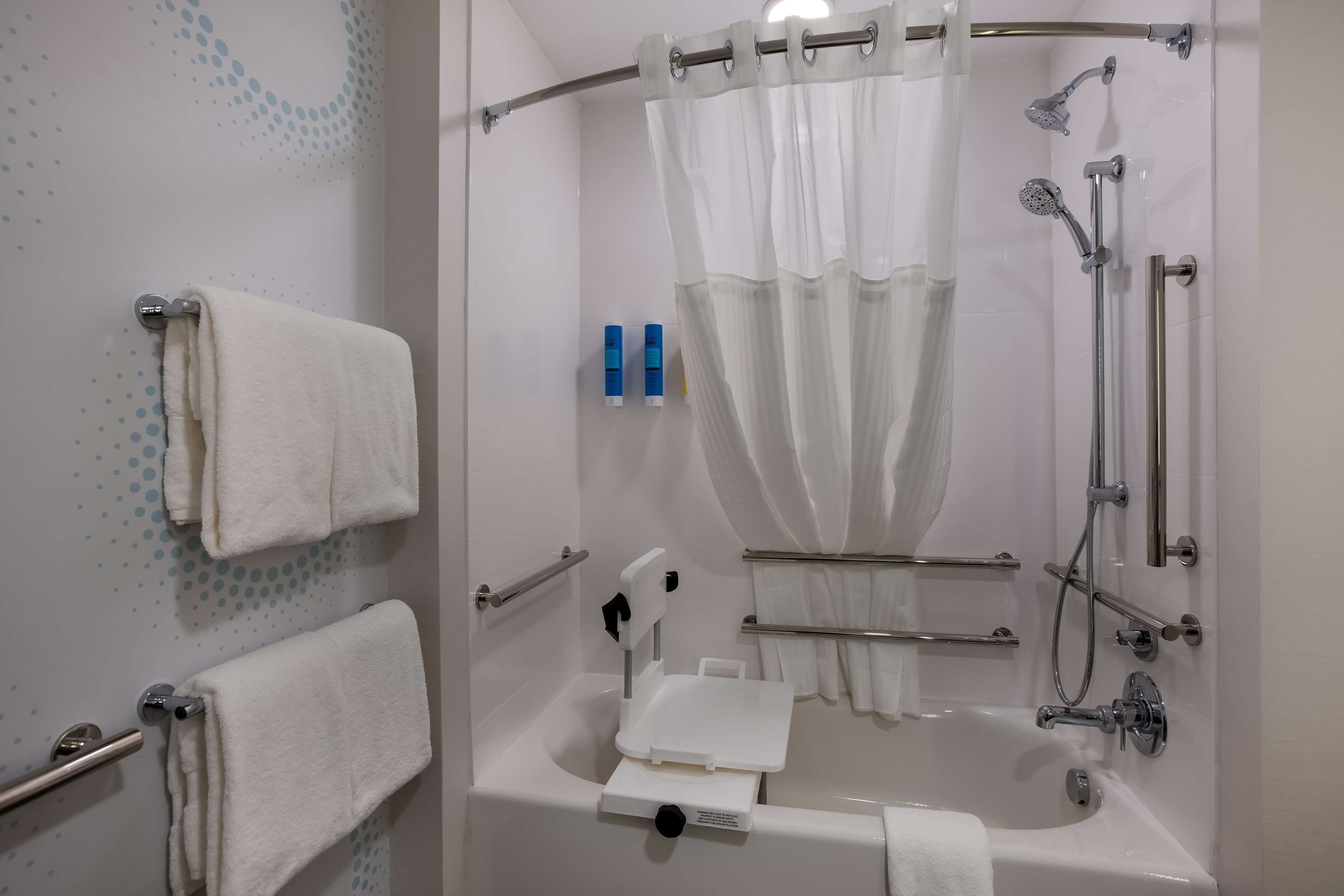 A modern bathroom with a bathtub, shower, and handrails.