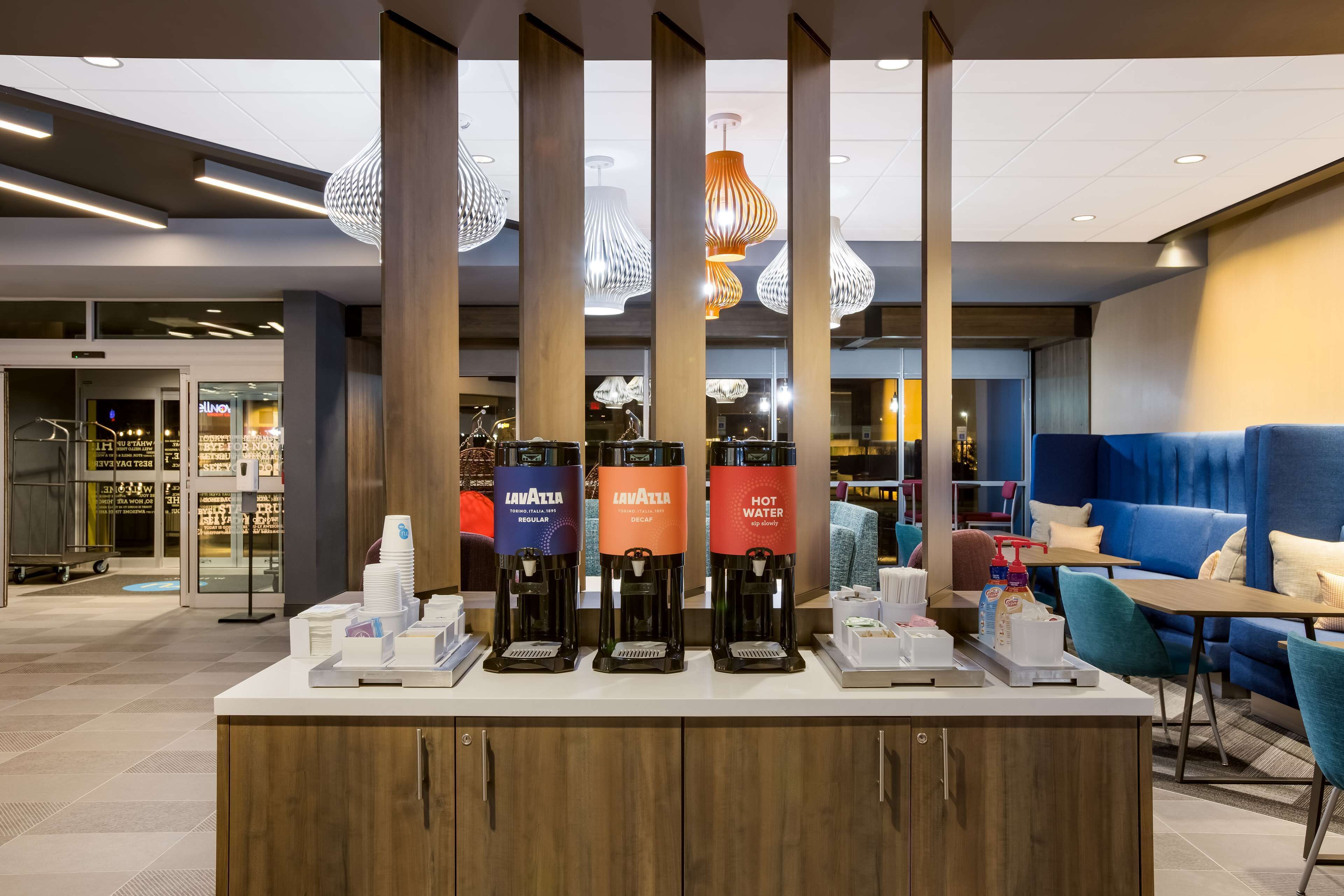 A hotel lobby with a coffee station, seating area, and a store in the background.