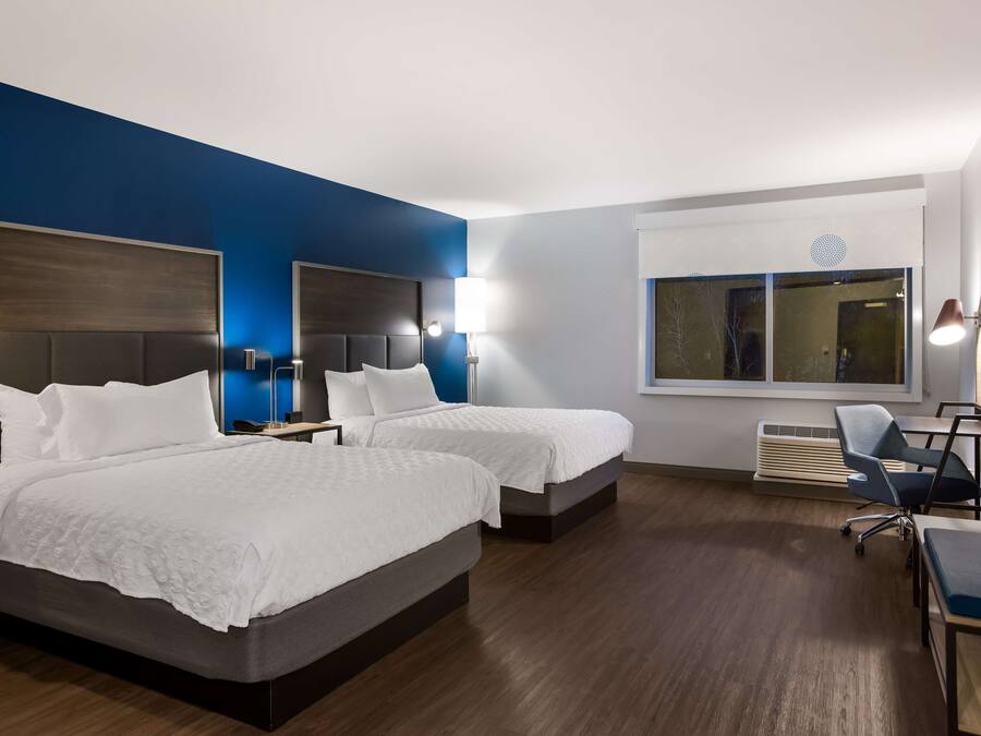 A hotel room with two beds, a desk, a chair, a TV, and a window.