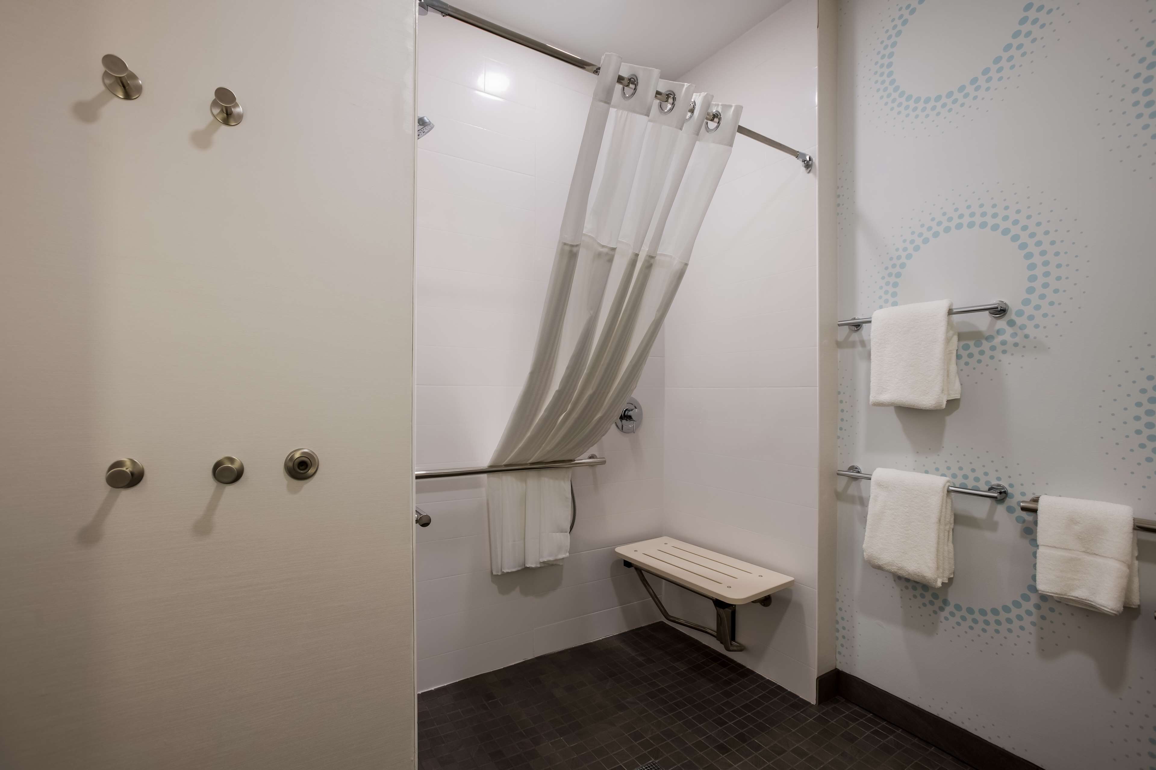 Een badkamer met een douche, een bankje en handdoekhouders.