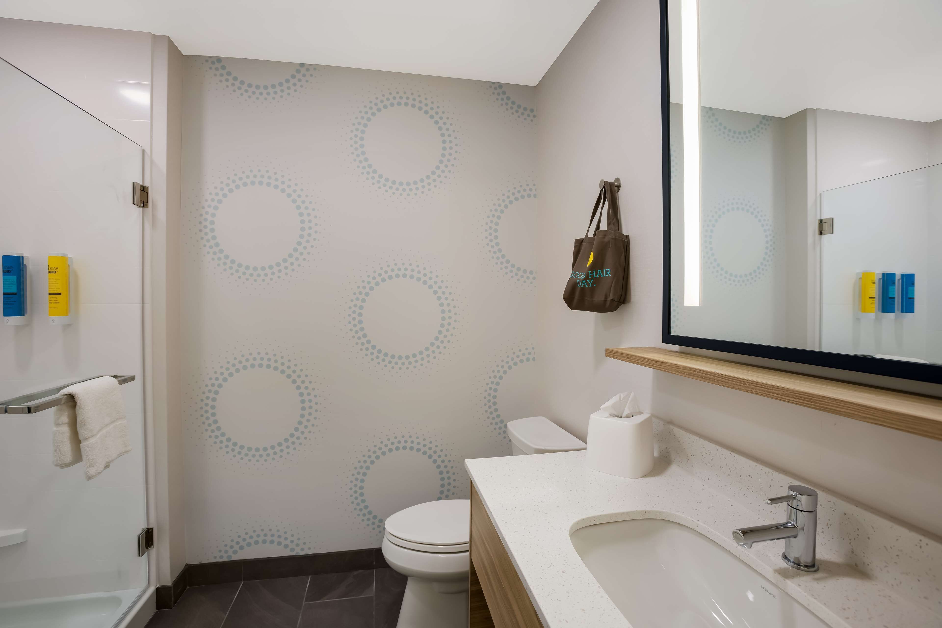 Ein modernes Badezimmer mit Toilette, Waschbecken und Dusche. Ein Handtuchhalter und eine Tasche sind sichtbar.