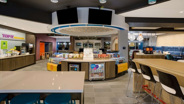 Un caffè moderno con un bancone centrale, area con posti a sedere e ingresso ben visibile.