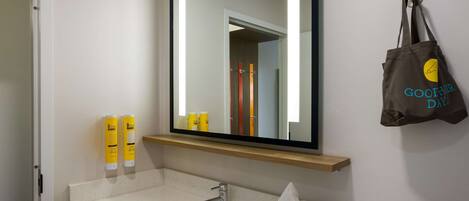 Un baño con lavamanos, espejo y artículos de aseo.