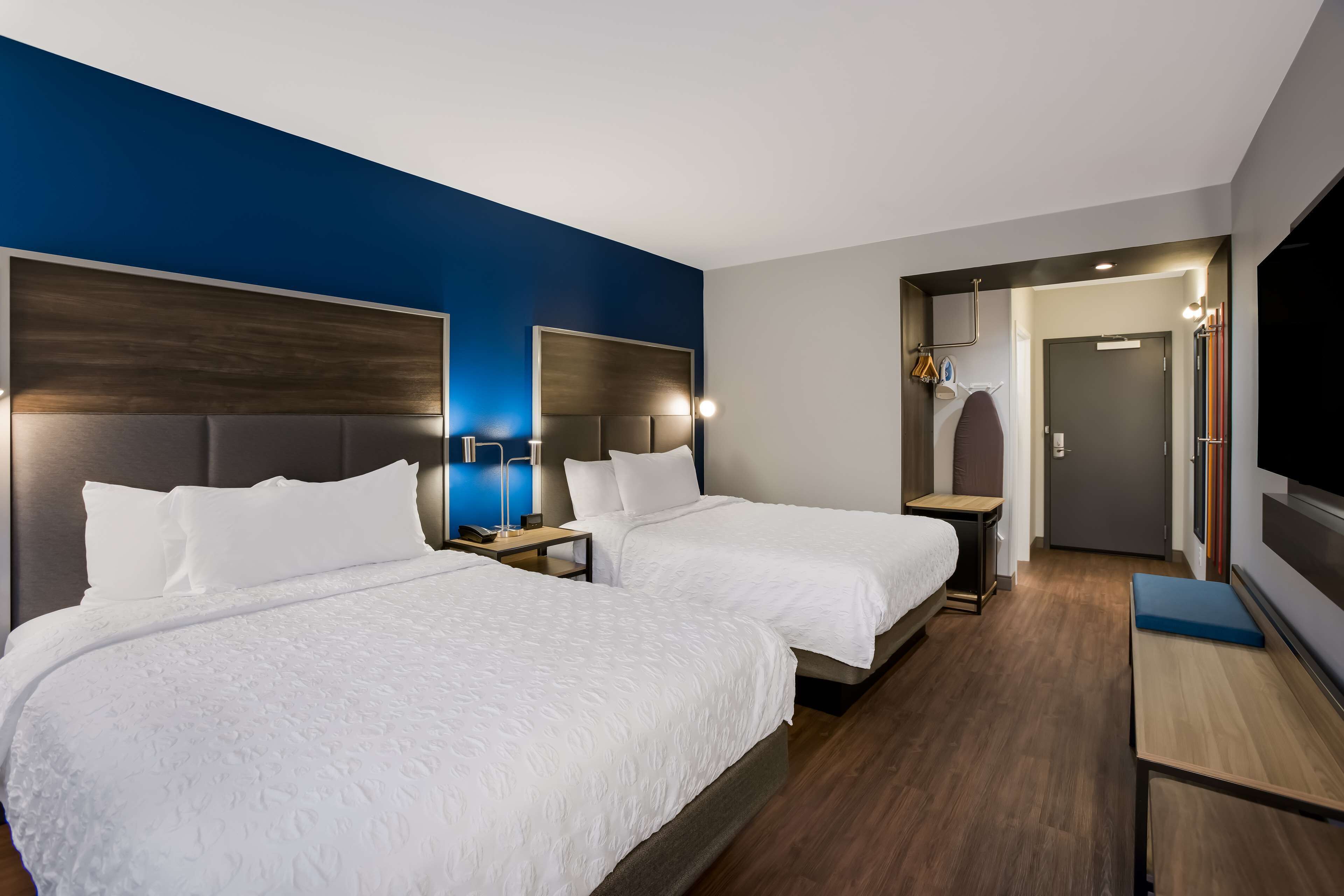 A hotel room with two beds, a TV, a desk, and a mirror.