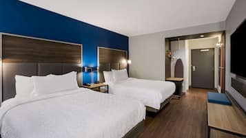 A hotel room with two beds, a TV, a desk, and a mirror.