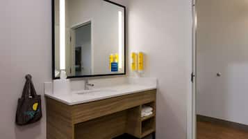 Une salle de bain moderne avec un lavabo blanc, un meuble-lavabo en bois et un grand miroir. On y trouve des articles de toilette sur le comptoir et un porte-serviettes.
