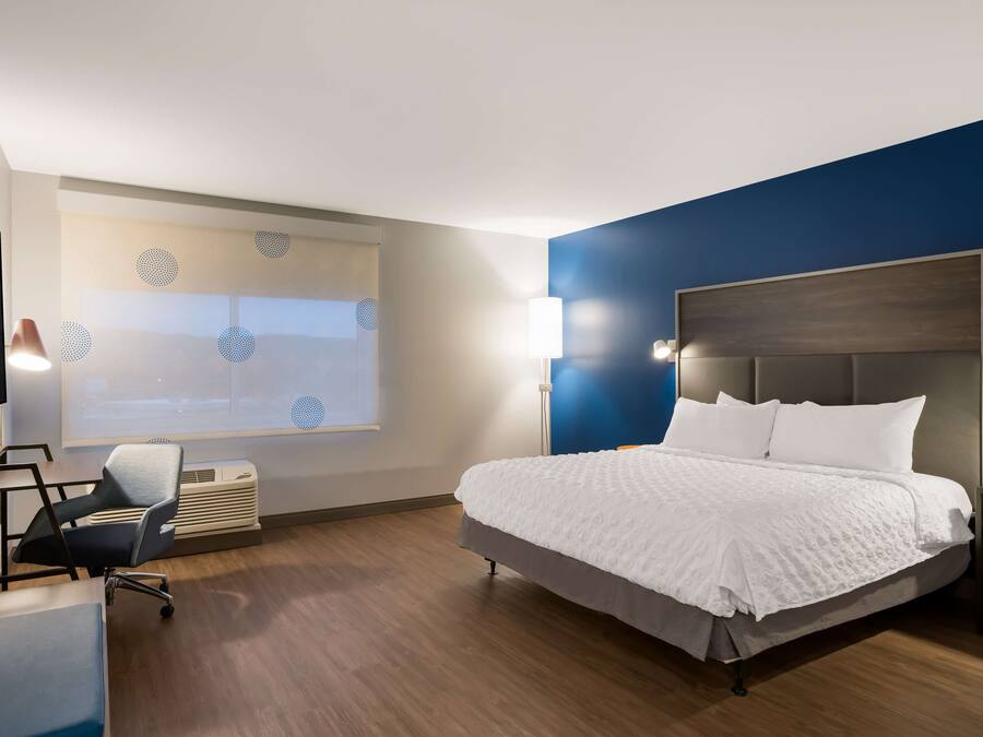 Habitación de hotel moderna con una cama grande, un escritorio, una silla y un amplio ventanal con vistas.
