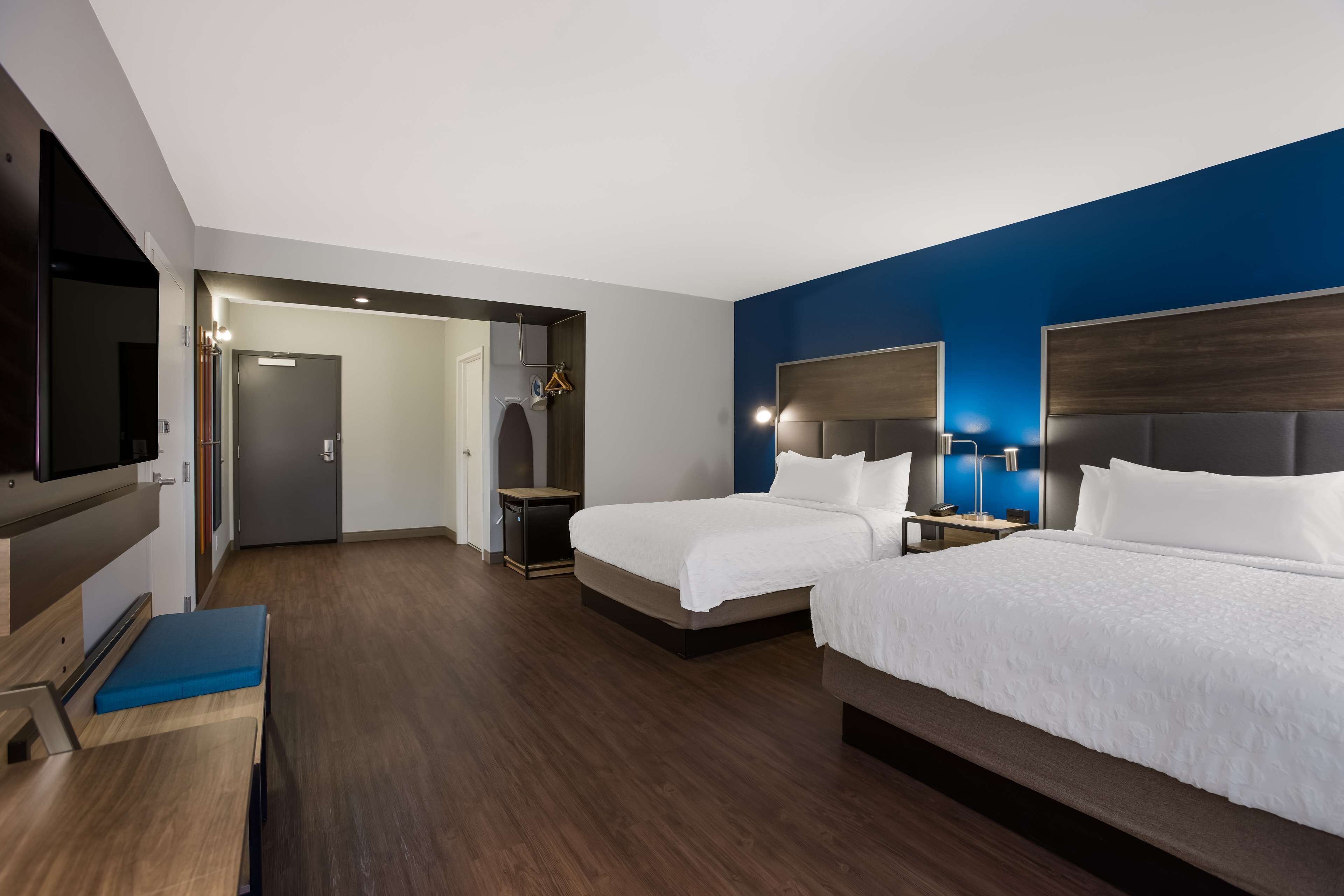 A hotel room with two beds, a TV, a desk, and a mirror.