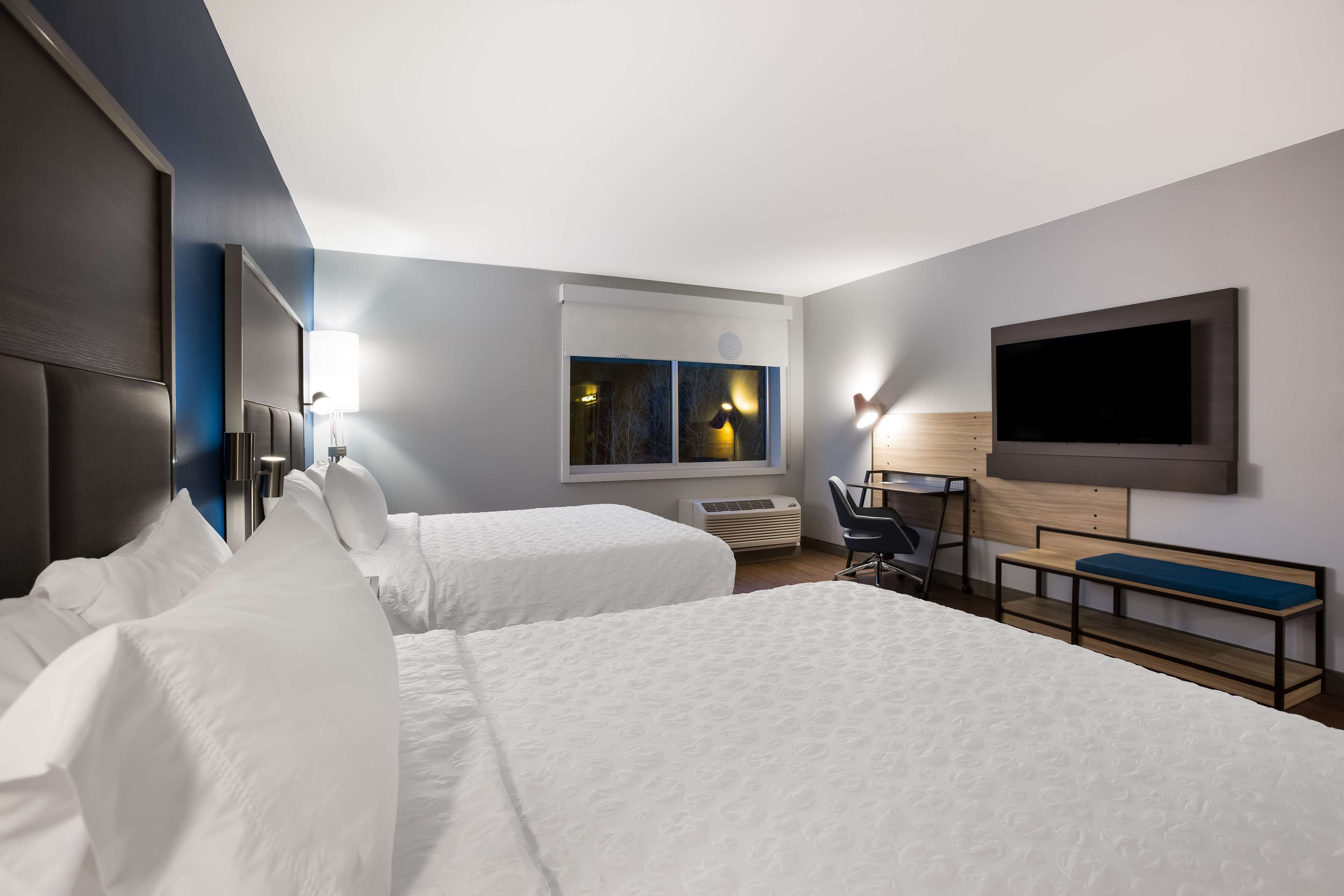 Habitación de hotel con dos camas, un escritorio, una silla, un televisor y una ventana con vistas.