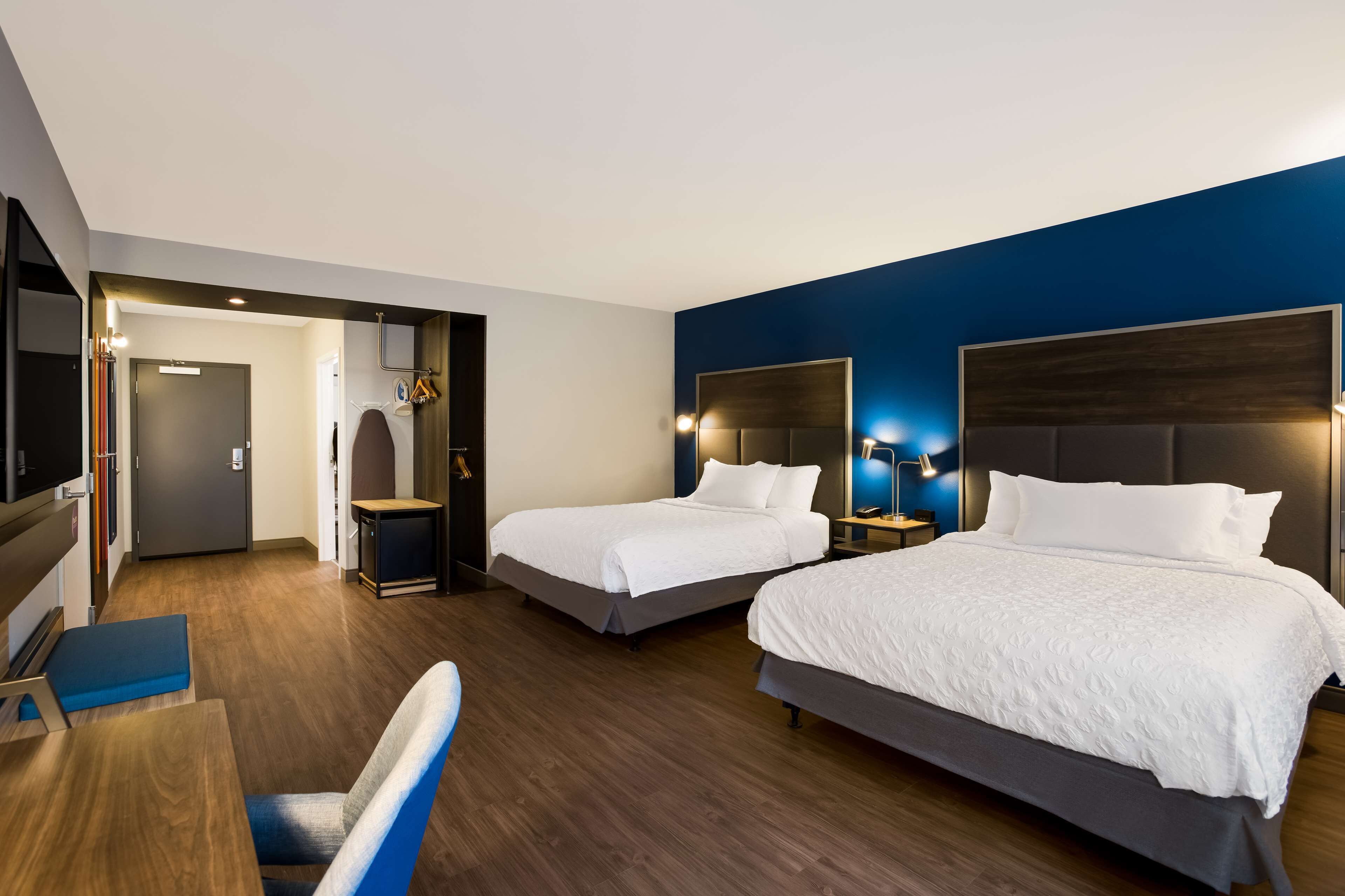 A hotel room with two beds, a desk, and a chair.
