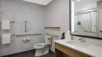 A modern bathroom with a toilet, handrails, a sink, and a mirror.