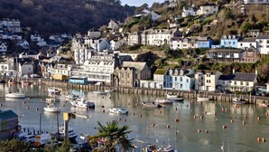 A coastal town with a marina filled with boats, houses on a hillside, and a clear sky. - A bright and spacious three bedroom house with panoramic views over Looe. (Looe)