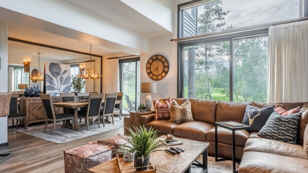 A spacious living room with a leather sofa, a wooden coffee table with a plant, and a dining area with a large mirror and chandelier. - On Golf Course Fully Renovated Luxury 4 Bedrm 3 Full Bathrms and Half Bath Snowcreek 732 Phase V (Mammoth Lakes)