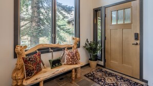 A wooden bench with animal-shaped cushions, a potted plant, and a patterned rug in a well-lit entryway with a wooden door and large windows. - On Golf Course Fully Renovated Luxury 4 Bedrm 3 Full Bathrms and Half Bath Snowcreek 732 Phase V (Mammoth Lakes)