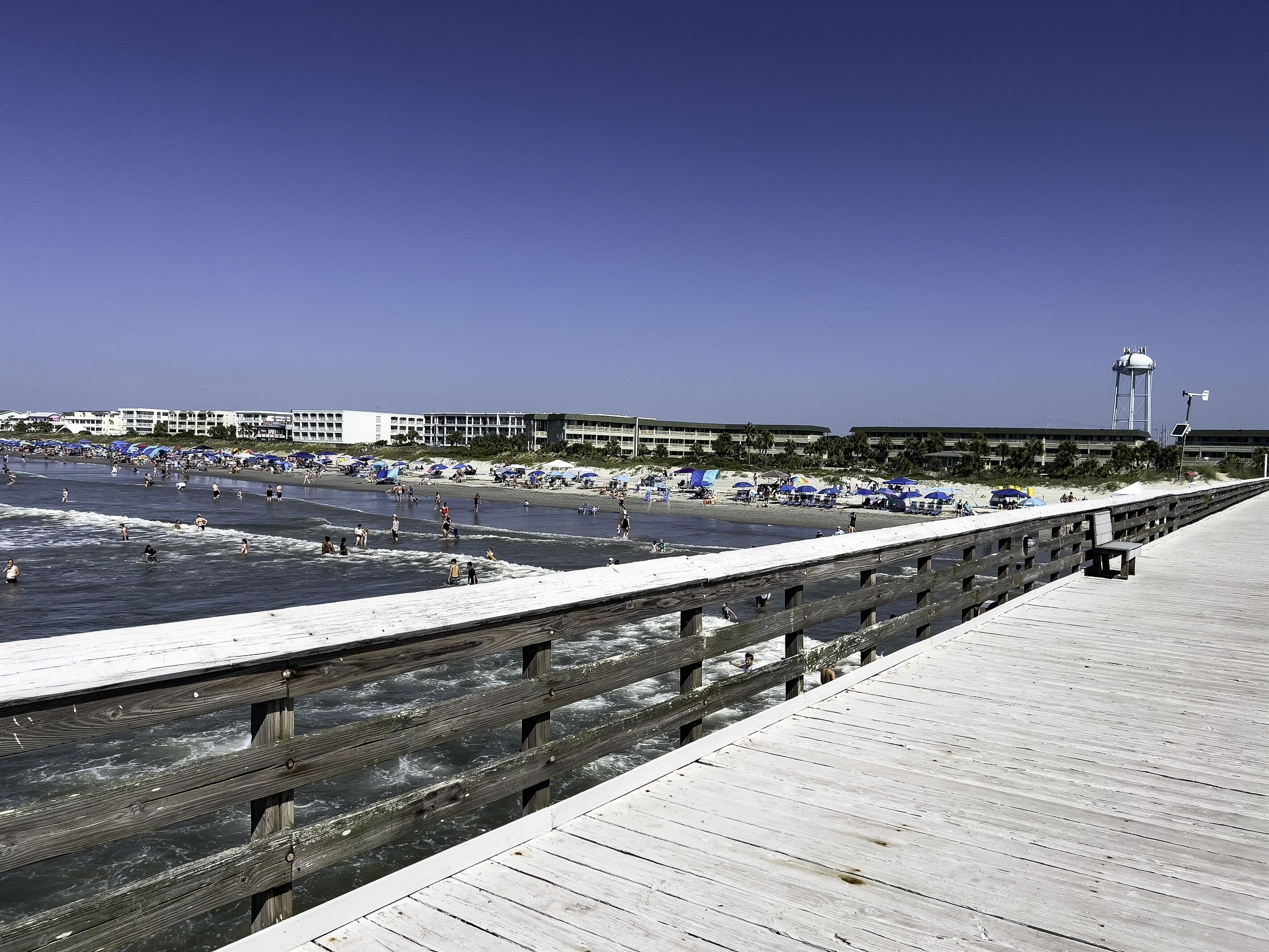 Une plage avec une promenade en bois, des parasols et des gens qui profitent de l’eau.