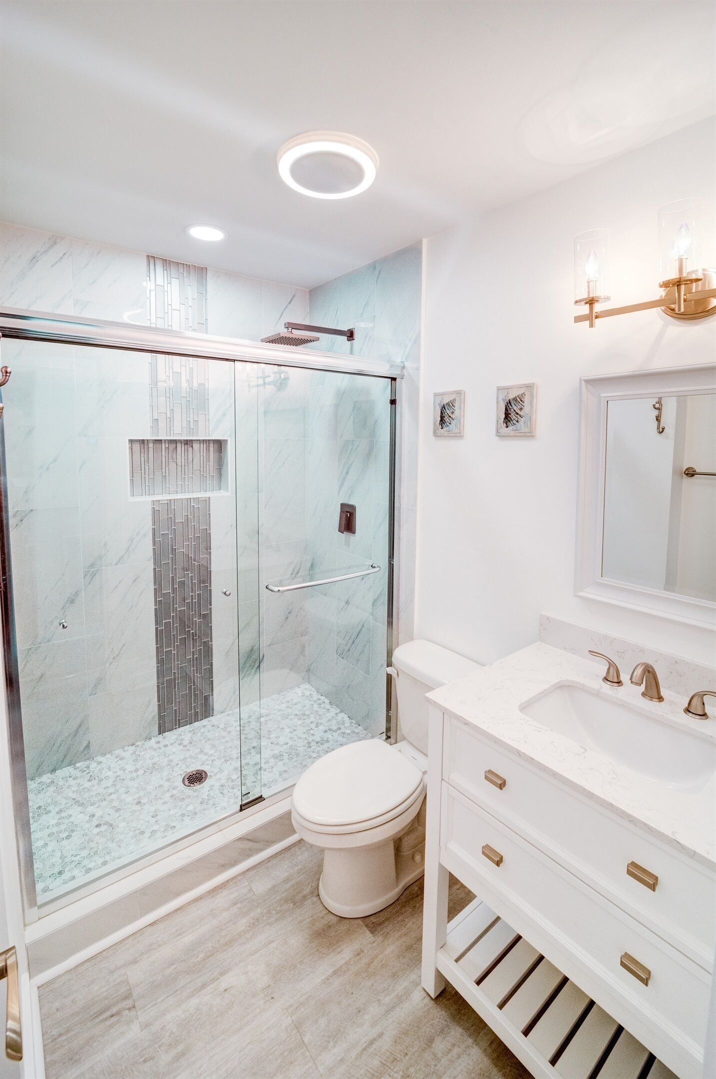 Un baño moderno con ducha de mampara de vidrio, inodoro blanco y tocador con detalles dorados.