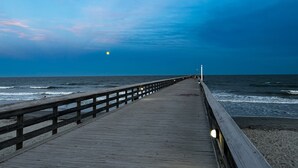 En træbro, der strækker sig ud i havet med gelænder på den ene side og en lysmast for enden.