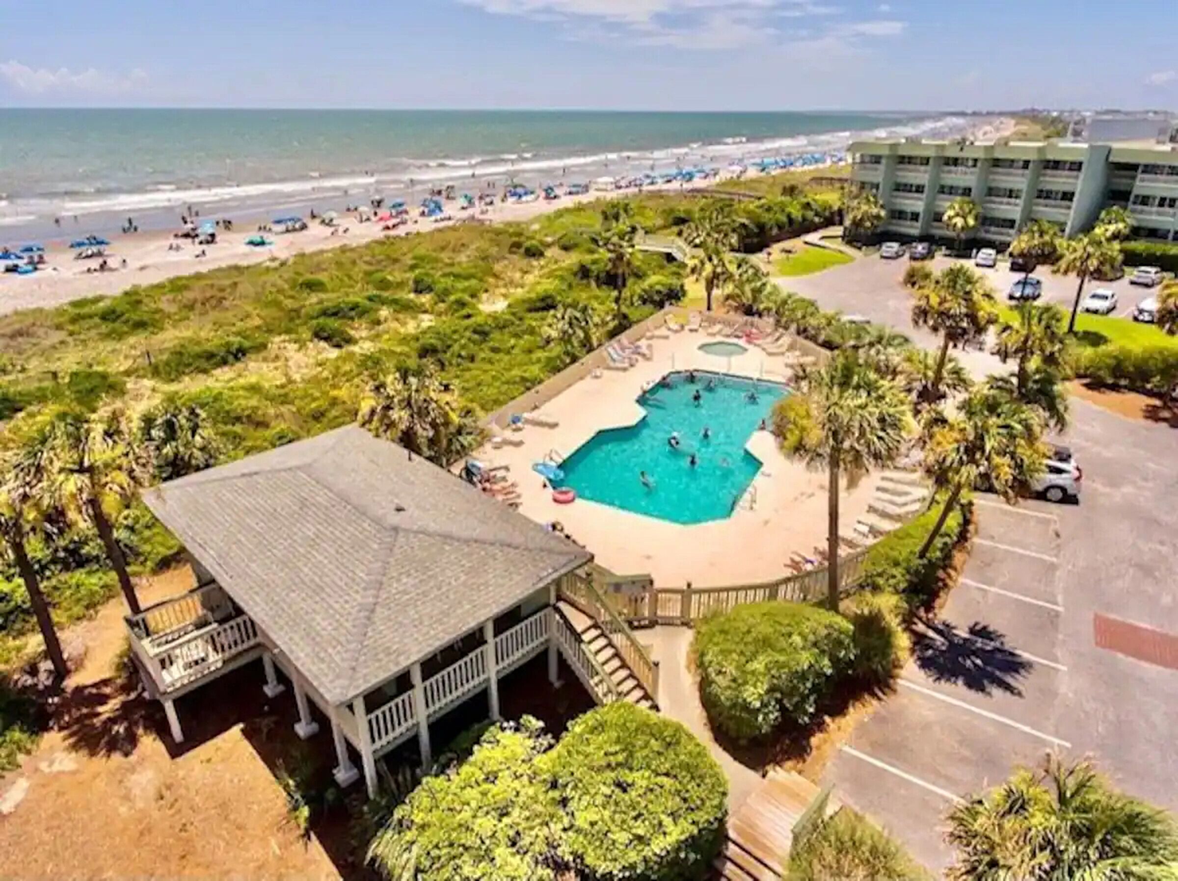 A resort with a swimming pool, beach, and parking area.