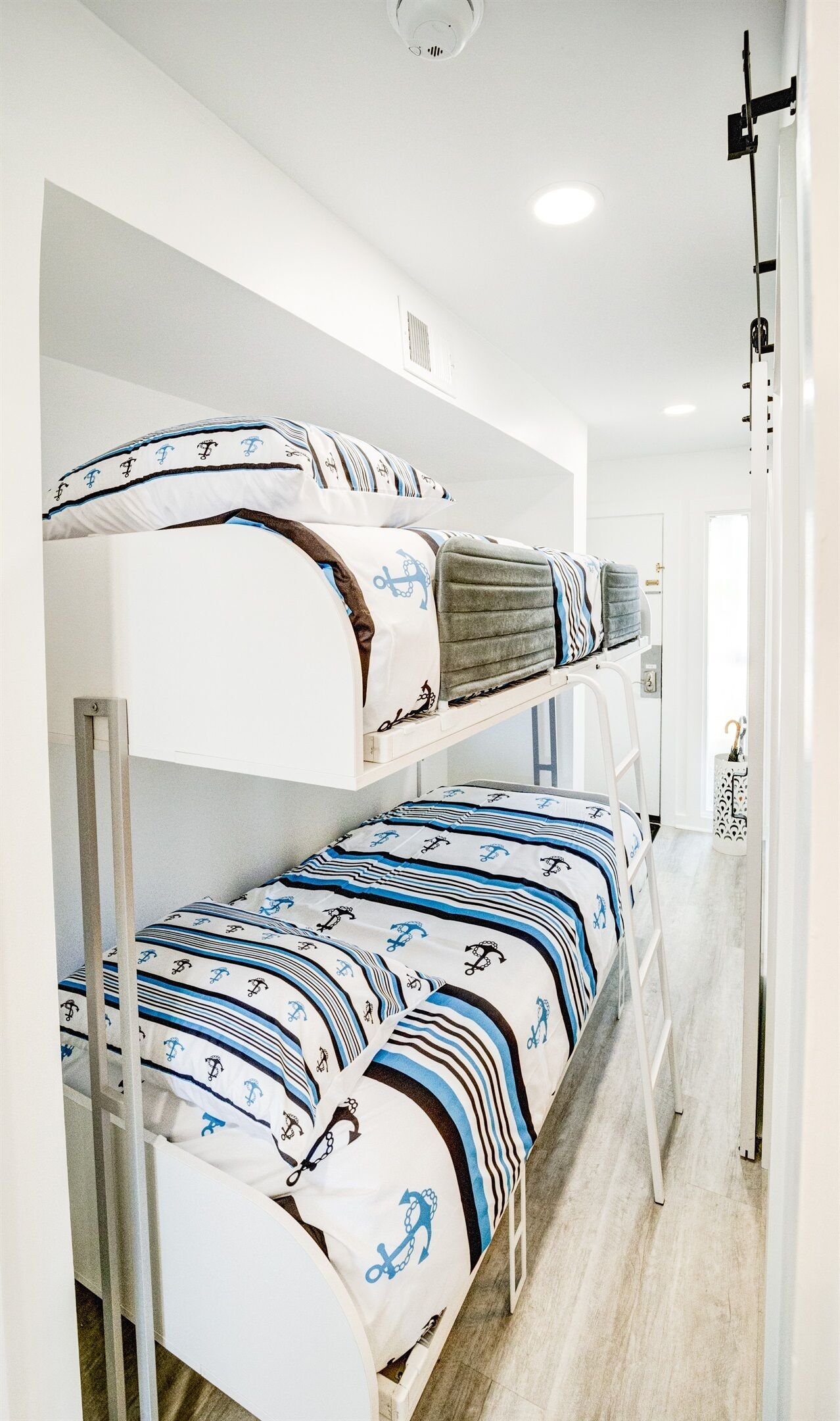 Una cama litera con ropa de cama de temática náutica en una habitación con paredes blancas y suelo de madera.