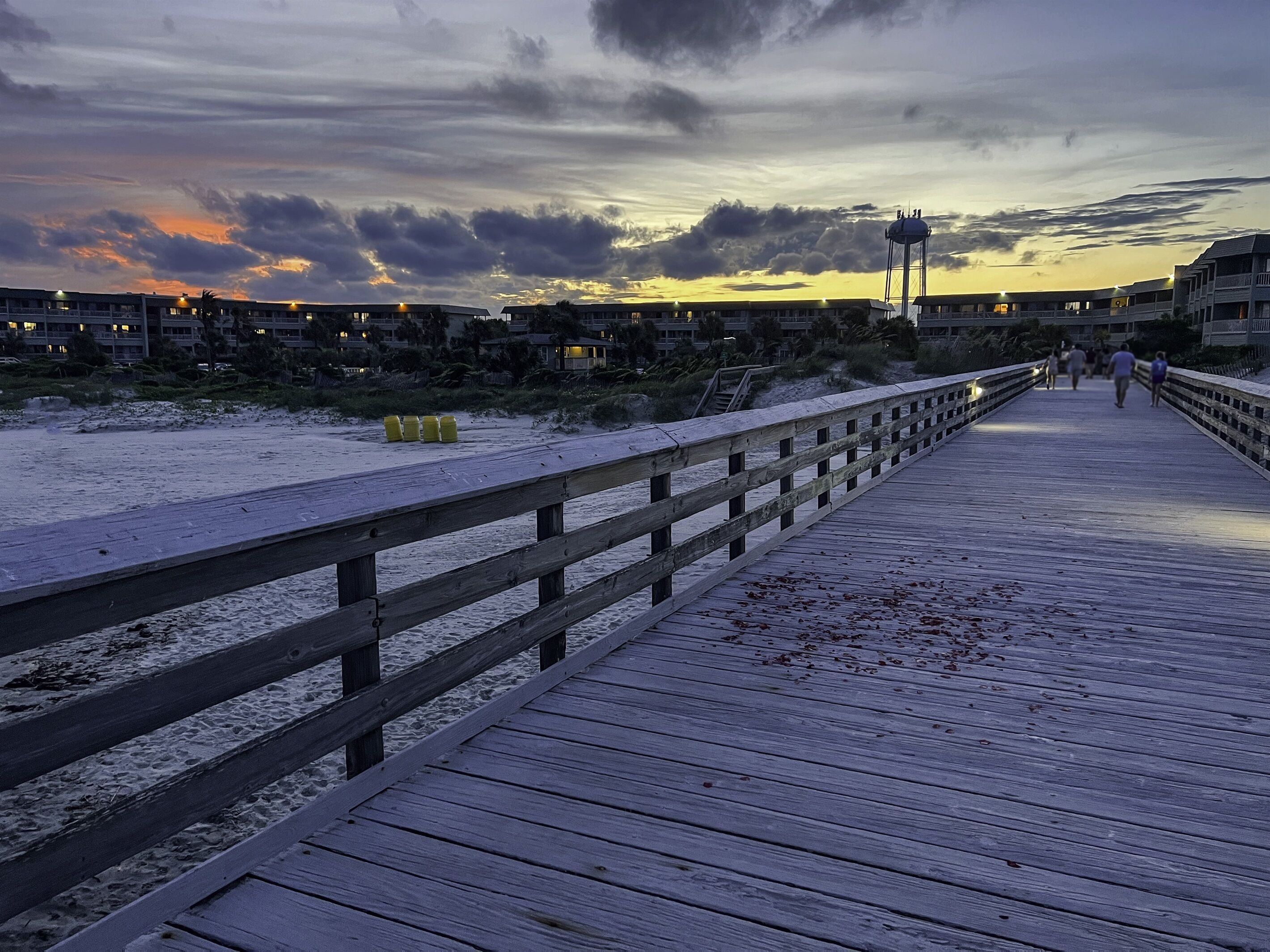 Une promenade en bois menant à une plage, avec un ciel nuageux en arrière-plan.