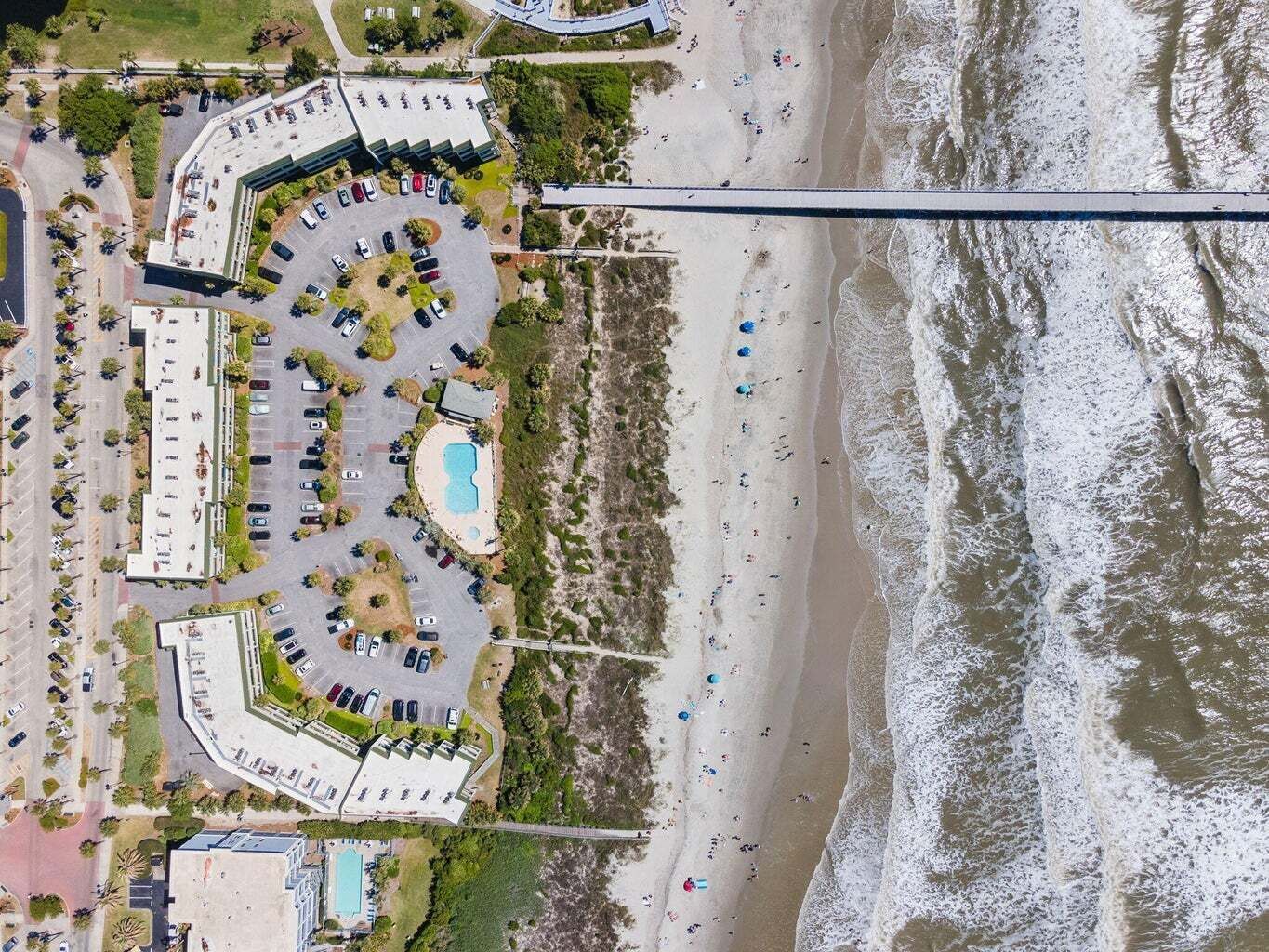 An aerial view of a coastal hotel with multiple parking lots, a swimming pool, and a beach.