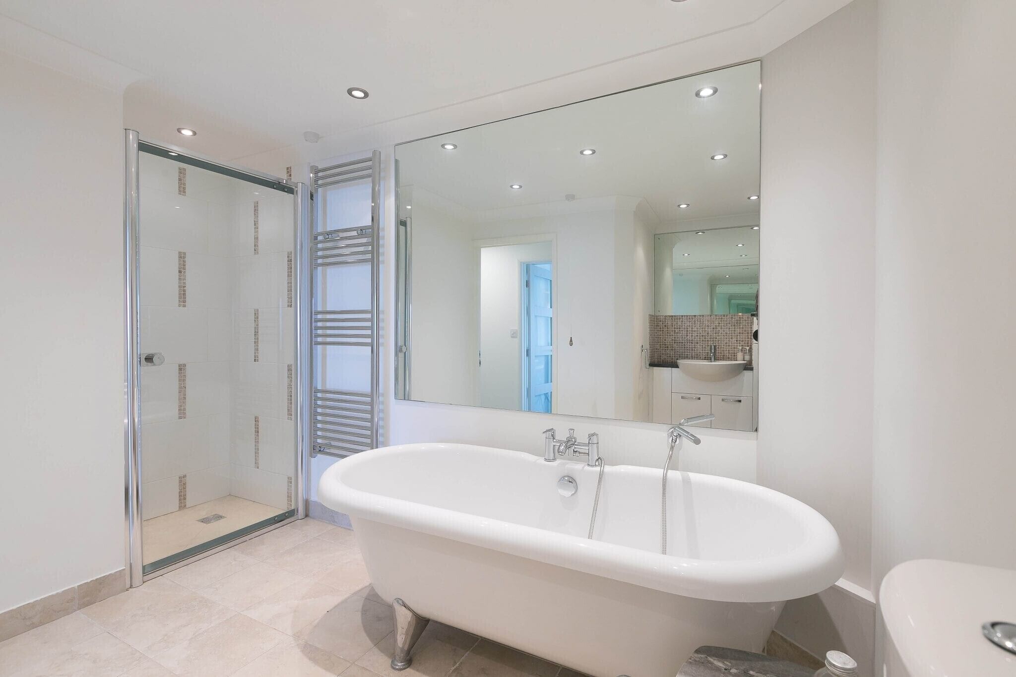 Un baño moderno con una bañera independiente, una cabina de ducha con mampara de cristal y un espejo grande que refleja el espacio.
