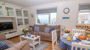 Una sala de estar con sofá, televisión, mesa de comedor con alimentos para el desayuno y vistas al exterior.