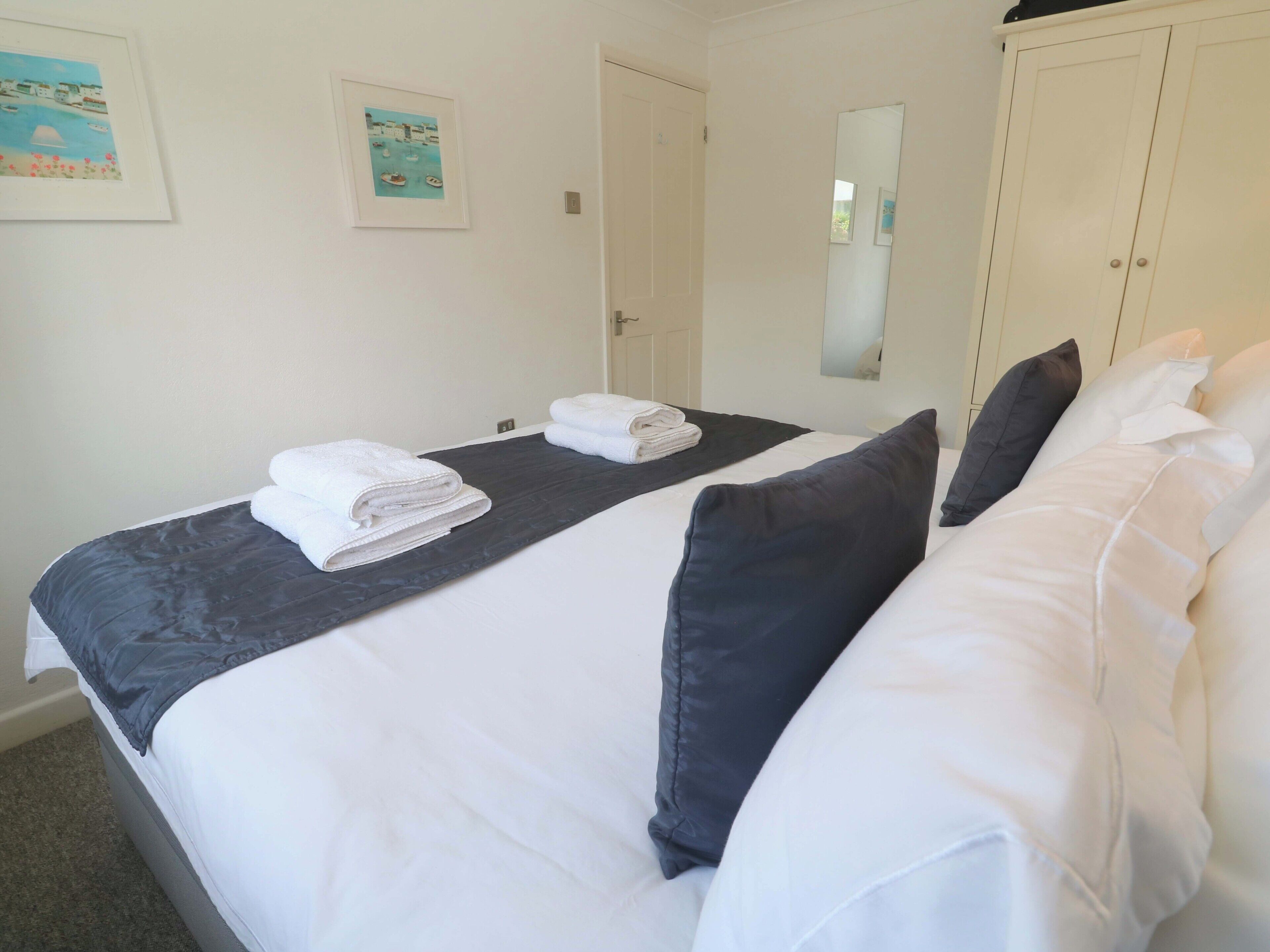 A hotel room with a bed, two pillows, a folded towel, a door, and a mirror.