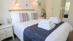 Una cama bien hecha con almohadas a rayas, una lámpara de noche y una pila de toallas dobladas.