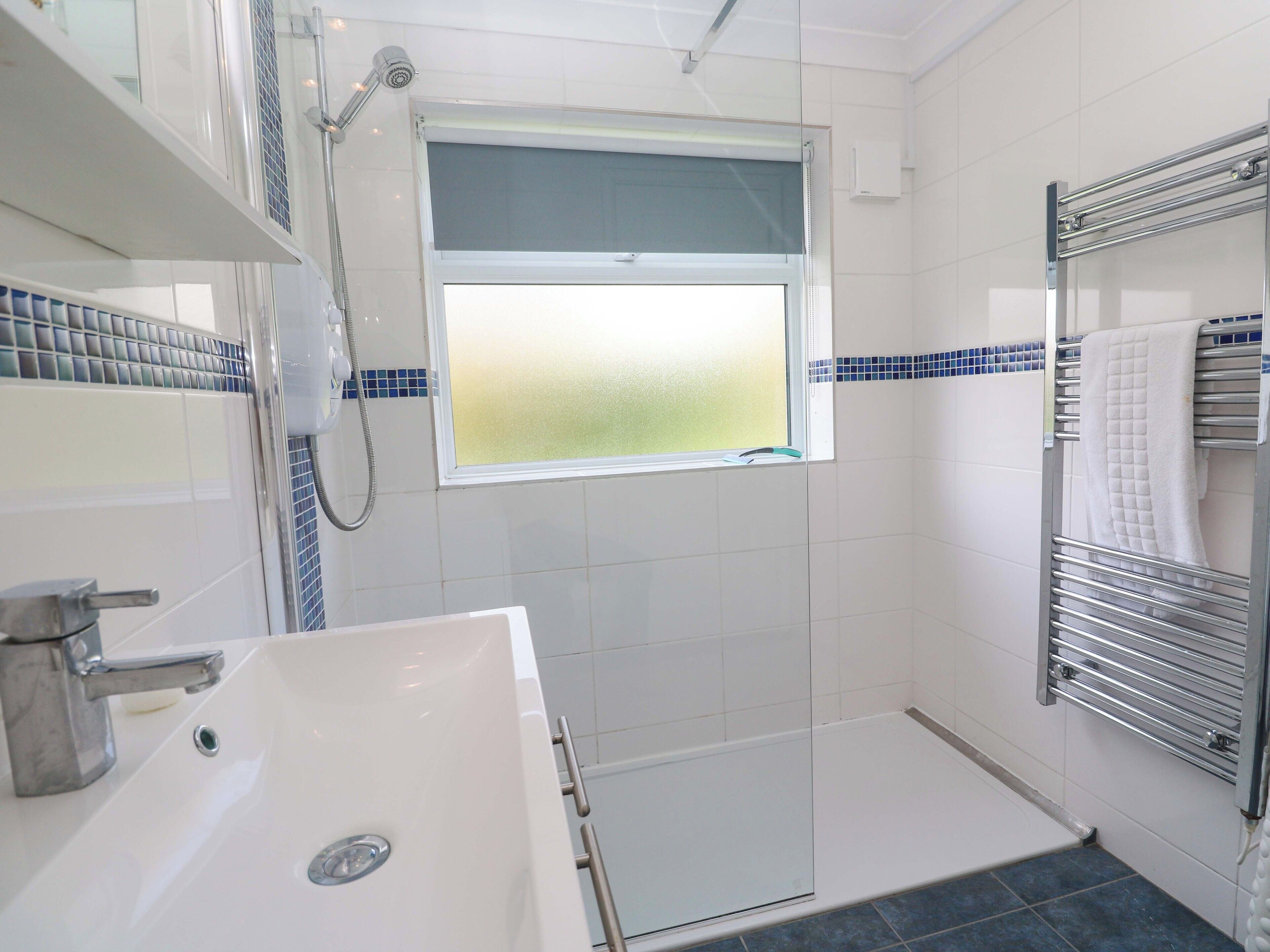 Ein Badezimmer mit einem weißen Waschbecken, einer Dusche mit Glastür und einem Fenster mit Blick.