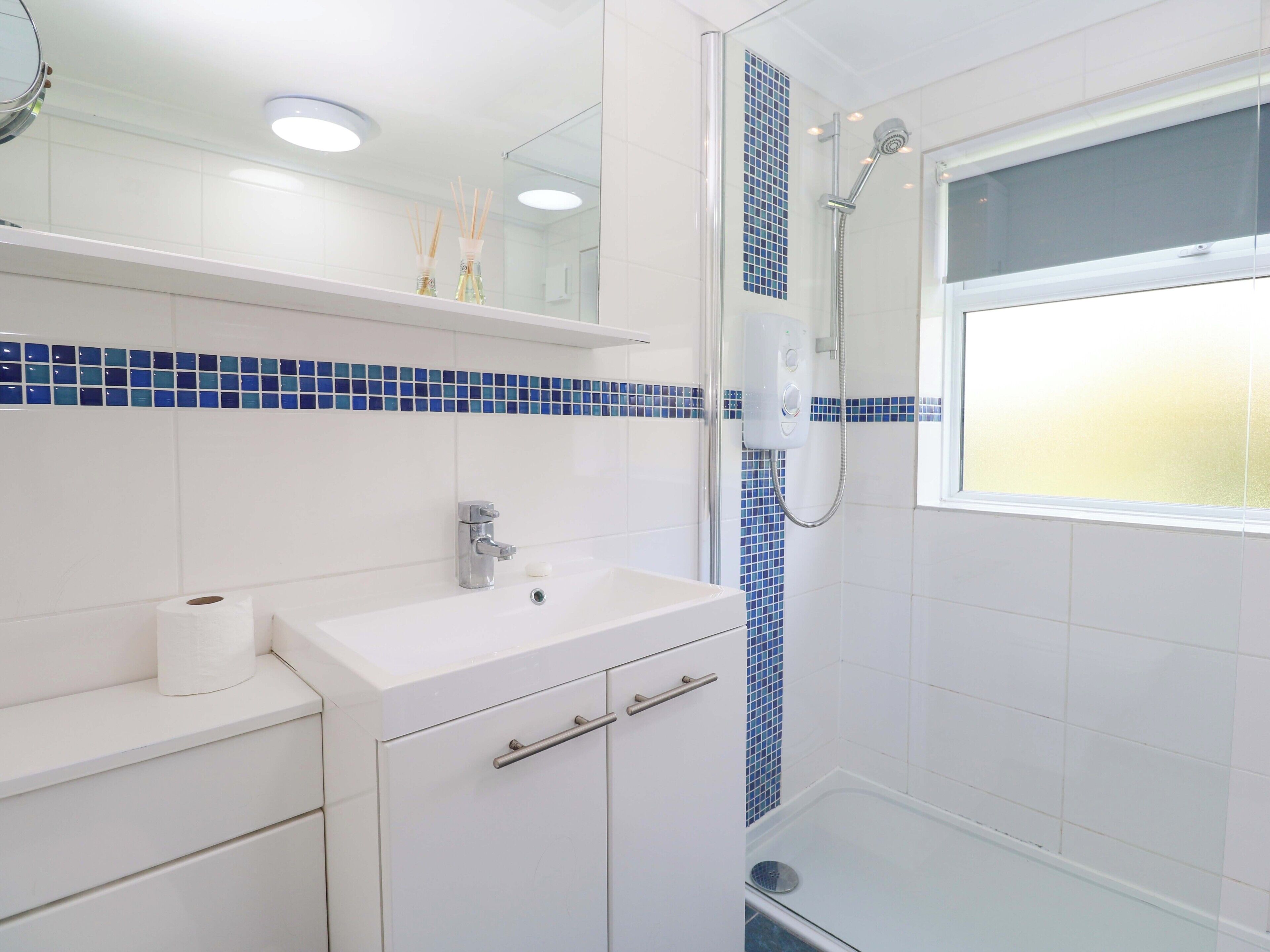 Un baño moderno con un lavabo, espejo y ducha blancos.