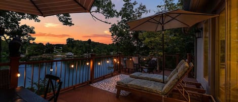 Une terrasse avec des sièges extérieurs, une vue sur un lac et un coucher de soleil.