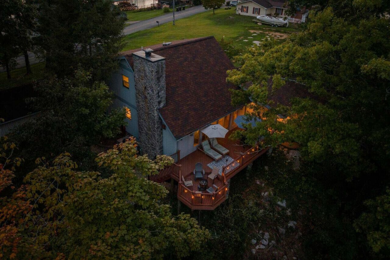 A house with a deck, a stone chimney, and a well-maintained lawn.