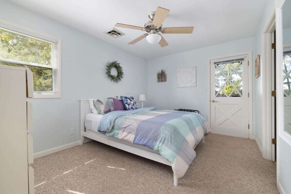 A bedroom with a bed, a ceiling fan, a door, and a window.