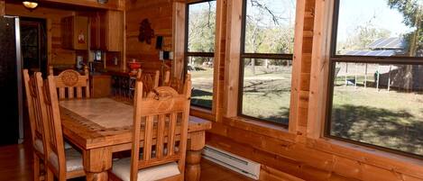 A wooden cabin interior with a dining table, chairs, and large windows.