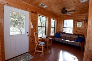 L’intérieur d’une cabane avec une porte en bois, un canapé, un fauteuil et une petite table.