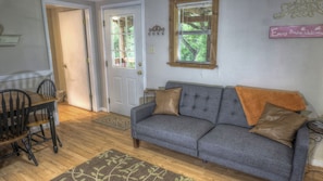 Un salon chaleureux avec un canapé gris, deux coussins marron, une table basse en bois et une petite table d’appoint.