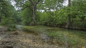 A river flowing through a forested area with trees and rocks along the banks. - Old Glory River Cabin (Utopia)