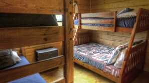 A bunk bed room with a wooden floor, a small storage box, and a quilted bedspread. - Old Glory River Cabin (Utopia)