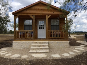A wooden cabin with a porch, a front door, and two windows.
