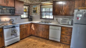 A kitchen with wooden cabinets, a stove, a microwave, a sink, and a refrigerator. - Rock N Utopia (Utopia)