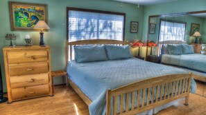 A bedroom with a wooden bed, a dresser, a window with blinds, and a mirror.